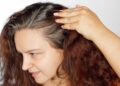 Woman showing graying hair roots by pushing left side of hair back