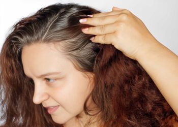 Woman showing graying hair roots by pushing left side of hair back