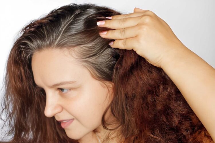 Woman showing graying hair roots by pushing left side of hair back