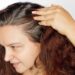 Woman showing graying hair roots by pushing left side of hair back