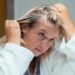 Woman checking scalp or hair parting in mirror