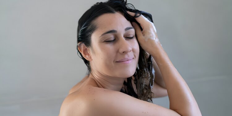 Happy young woman washing hair at home bathroom