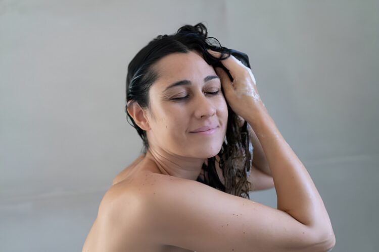 Happy young woman washing hair at home bathroom