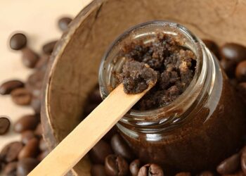 Homemade coffee scrub in a glass jar over coconut shell and coffee beans