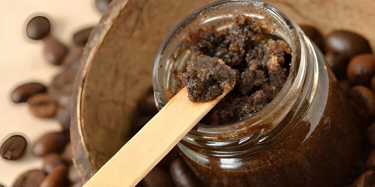 Homemade coffee scrub in a glass jar over coconut shell and coffee beans