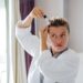 Middle-aged woman applies hair serum with a dropper to her scalp in front of a mirror