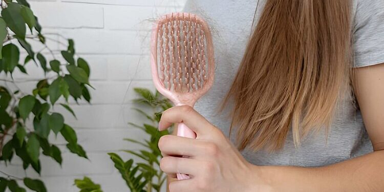 Woman holding pink hairbrush with fallen hair, hair loss problem