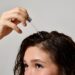 Woman applying hair oil with glass dropper to wet scalp