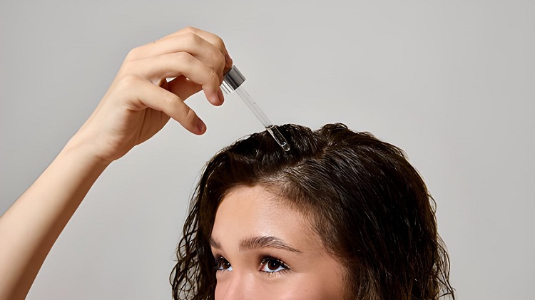 Woman applying hair oil with glass dropper to wet scalp