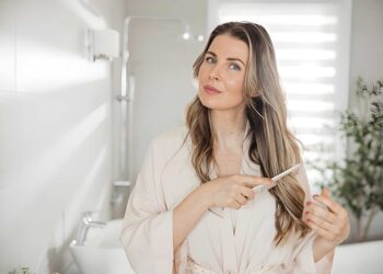 Woman brushing hair with comb while standing near mirror in bathroom