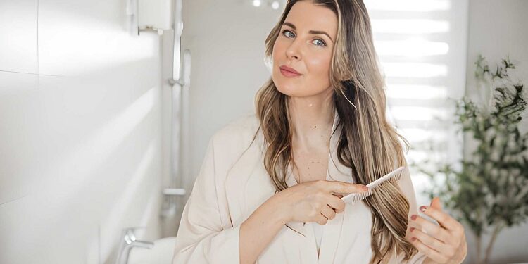 Woman brushing hair with comb while standing near mirror in bathroom