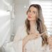 Woman brushing hair with comb while standing near mirror in bathroom