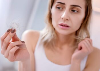 Sad unhappy woman looking at her hair while suffering from an illness